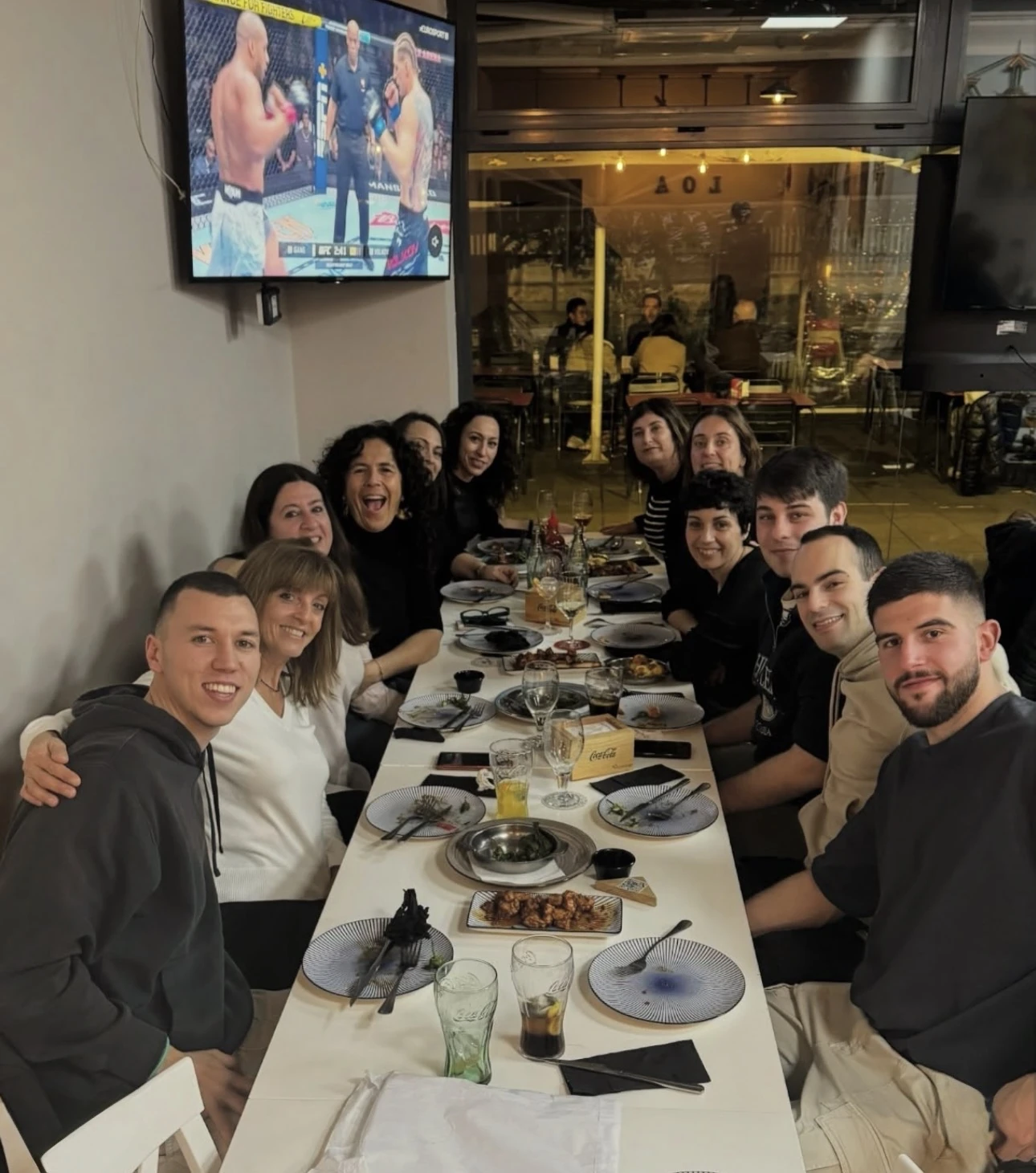 Grupo de clientes cenando en una mesa larga con un combate de UFC en la pantalla