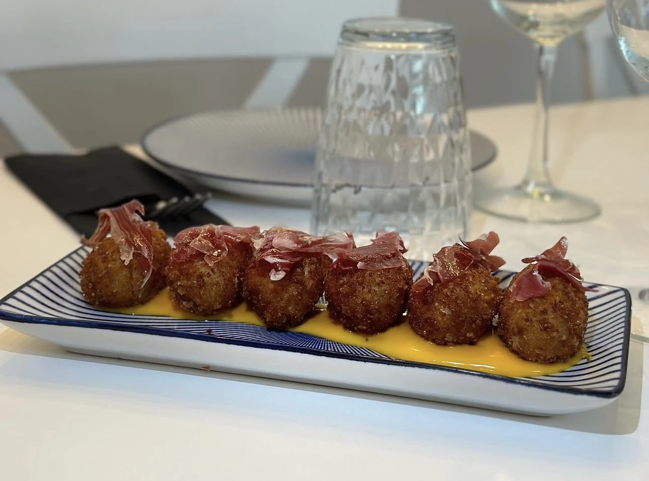 Croquetas con jamón ibérico sobre crema amarilla en plato azul y blanco