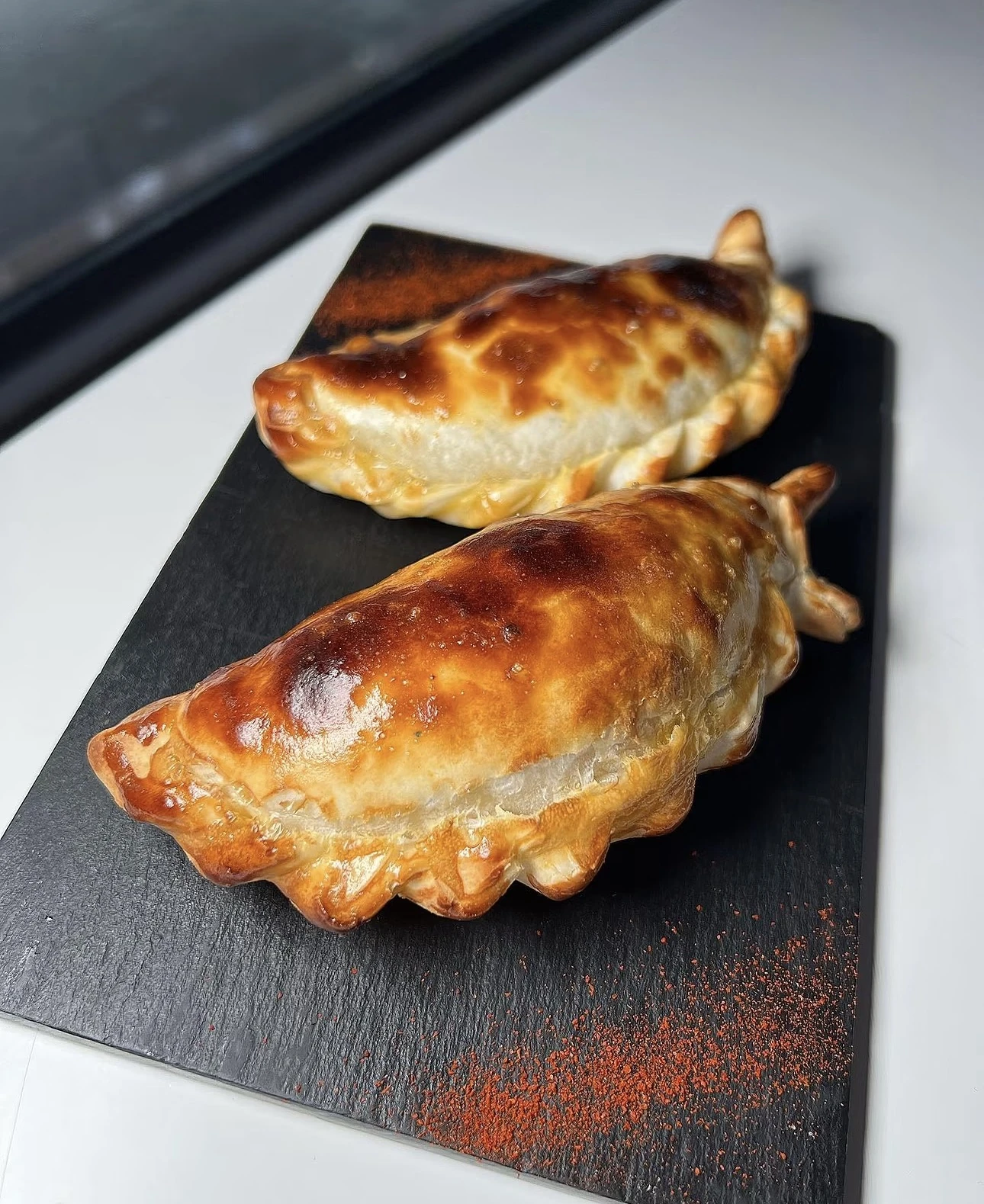 Dos empanadas argentinas doradas sobre pizarra negra con pimentón