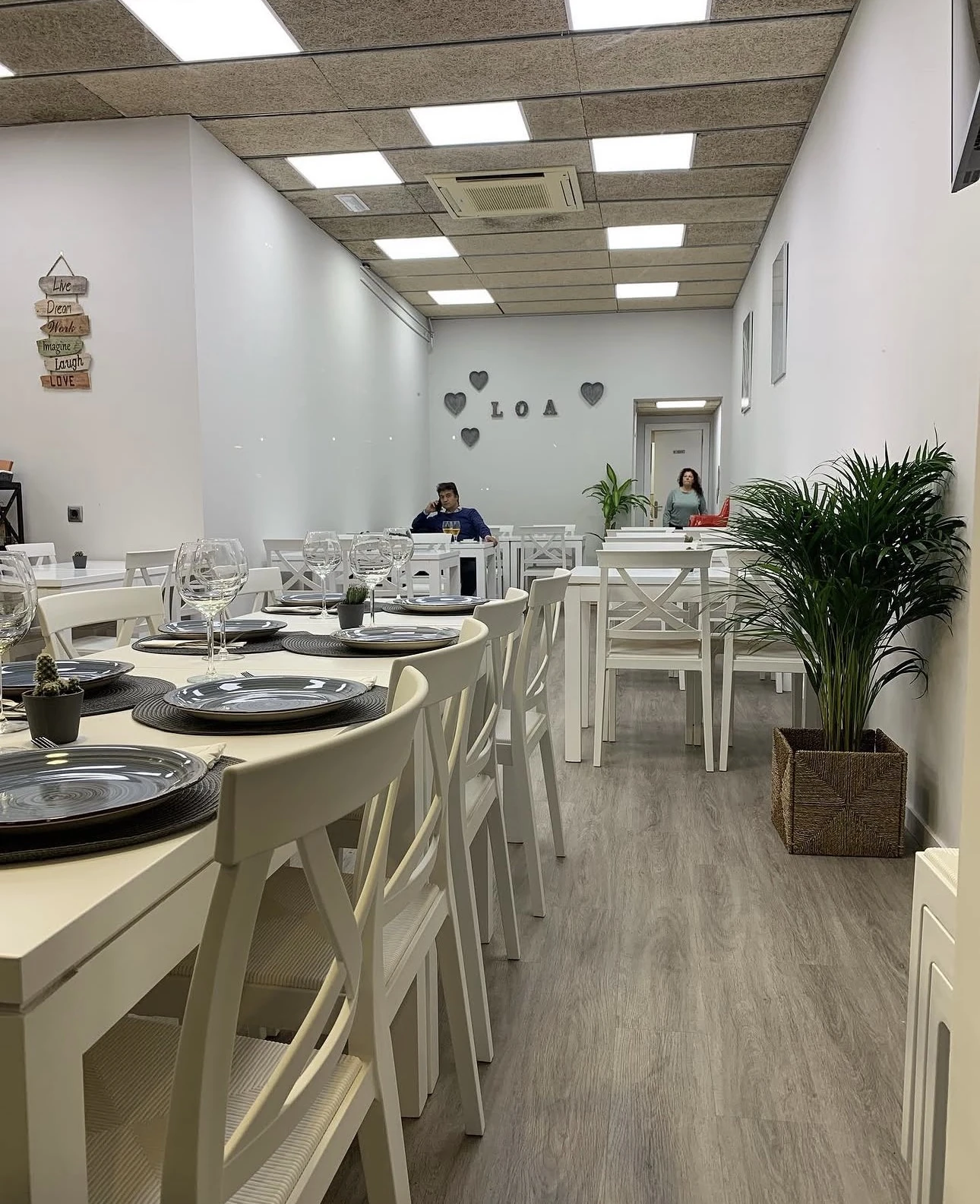 Sala del fondo de Barloa con mesas preparadas, plantas y letras LOA en la pared