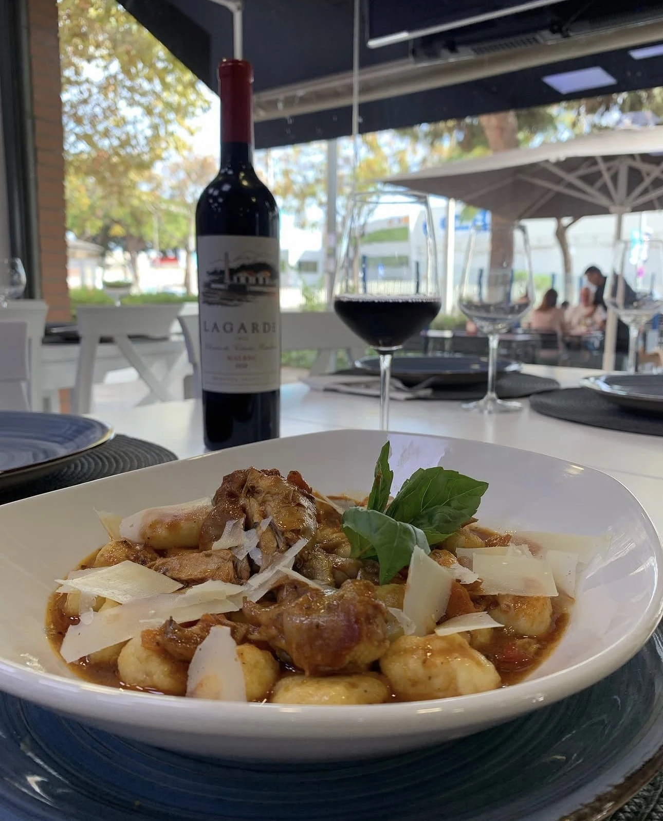 Plato de ñoquis con botella y copa de vino tinto en la terraza de Barloa